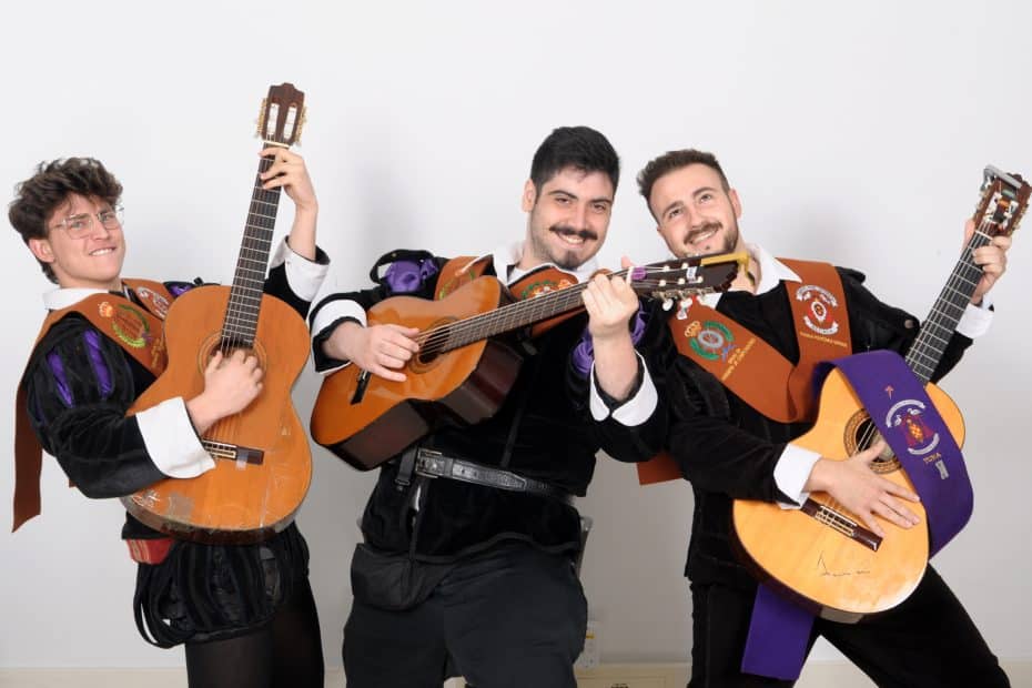 Tres tunos profesionales vestidos con trajes tradicionales y becas, posando con sus guitarras para contratación de eventos en contratartunas.net.